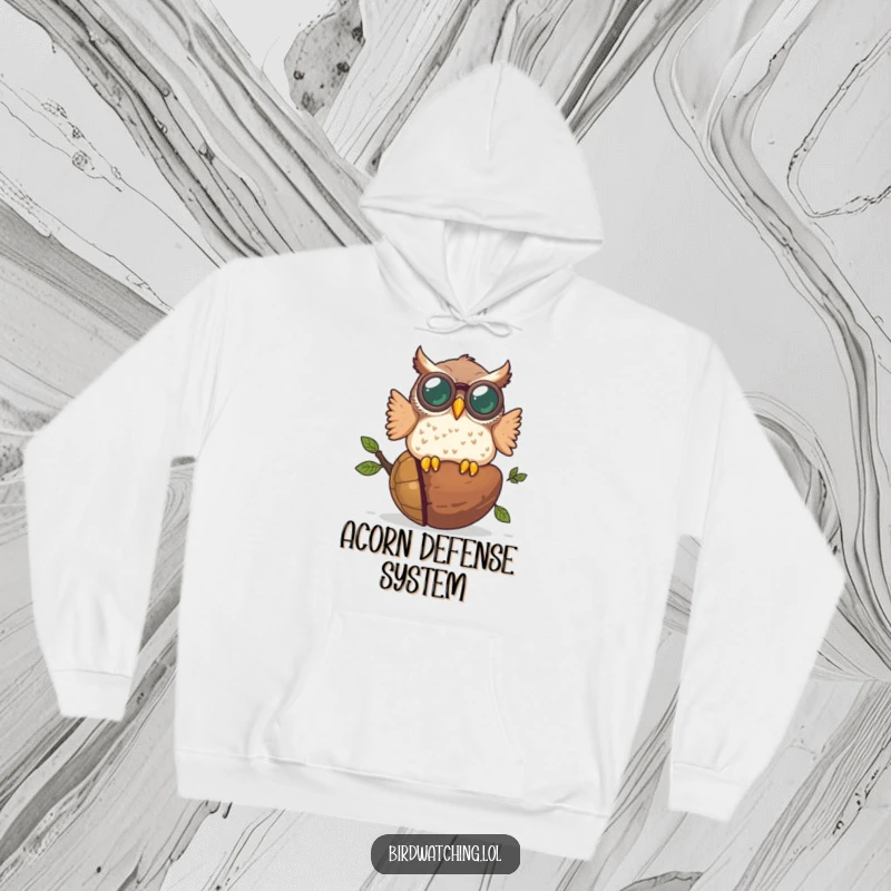 Funny hoodie showing a plump owl wearing huge binoculars colliding headfirst into a giant acorn, a scene of pure comedic disaster.
